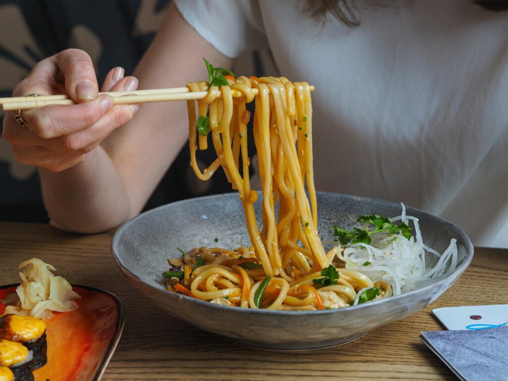 Close-up of a person using chopsticks to enjoy flavorful Asian noodles in a bowl.