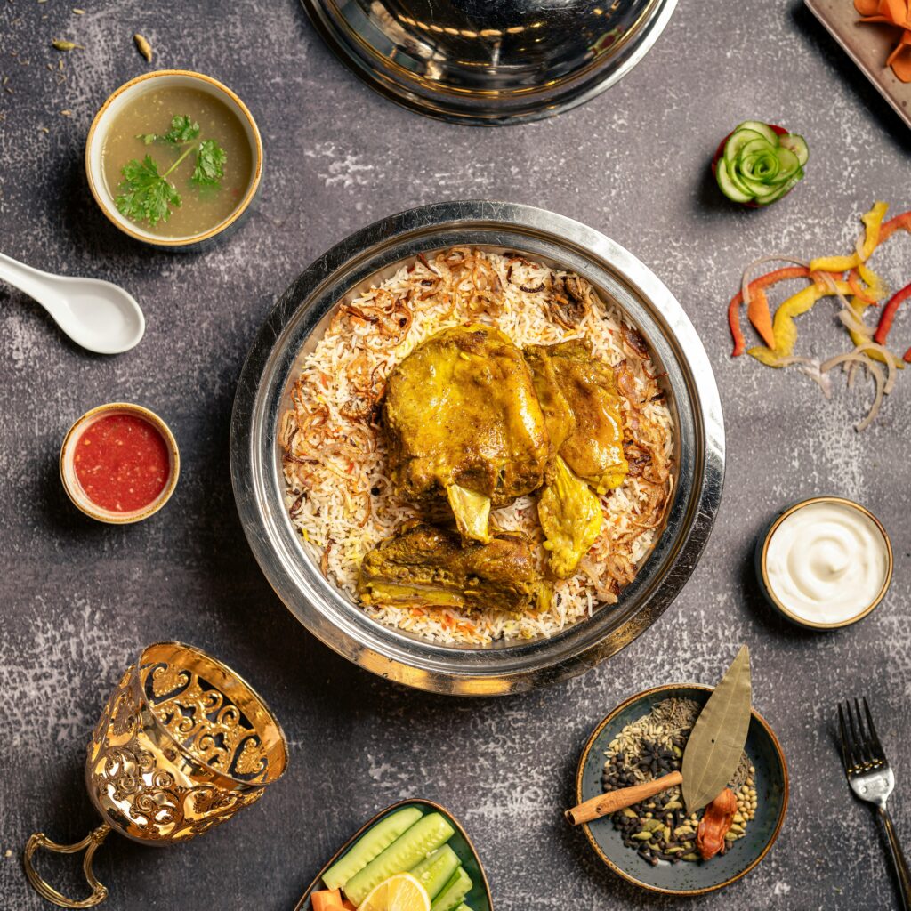Overhead view of a flavorful chicken mandi with traditional sides and garnishes on a textured surface.