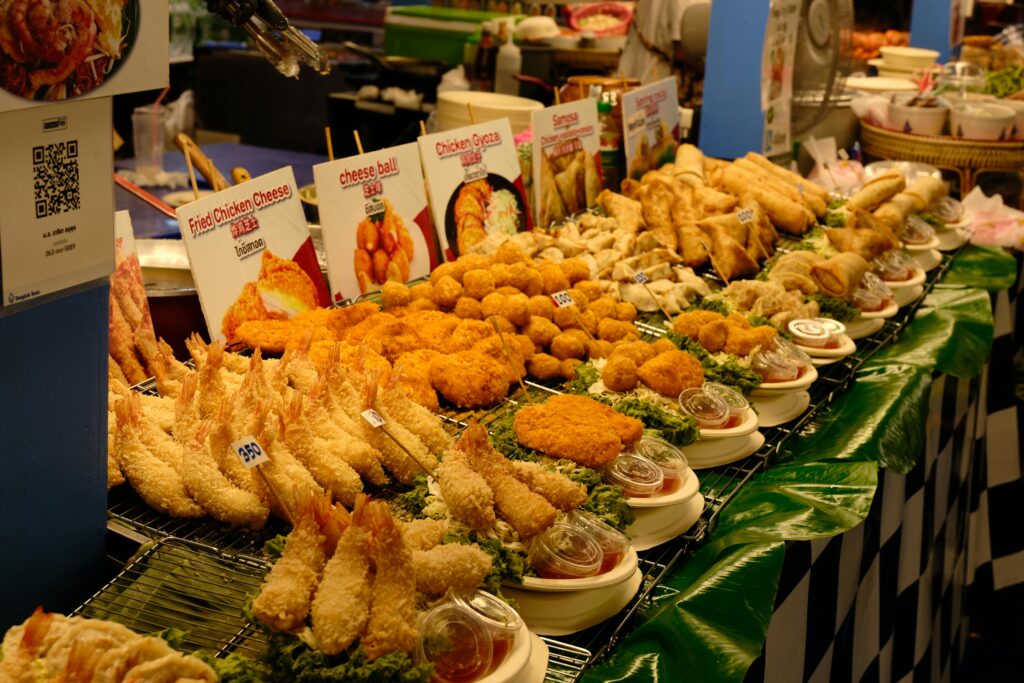 A vibrant display of various fried street foods, including shrimp, cheese balls, and spring rolls, at a food market.
