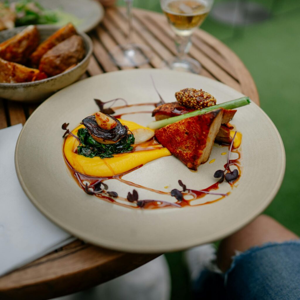 Exquisite gourmet dish artfully plated on a wooden table outdoors, highlighting culinary creativity.