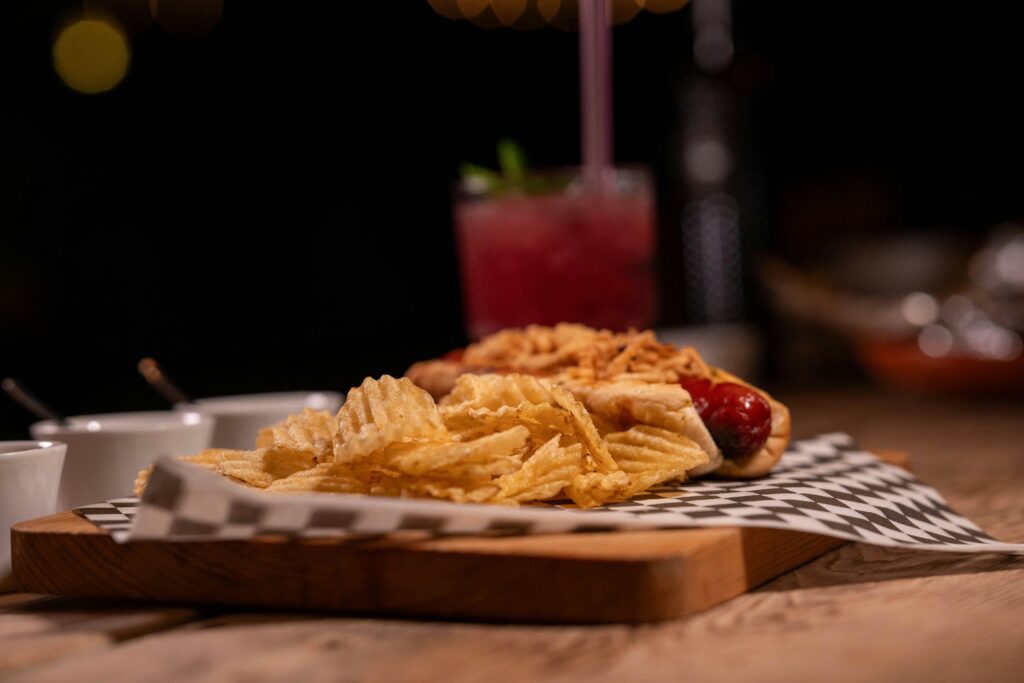 A tasty hot dog topped with crispy onions served with potato chips on a checkered napkin.