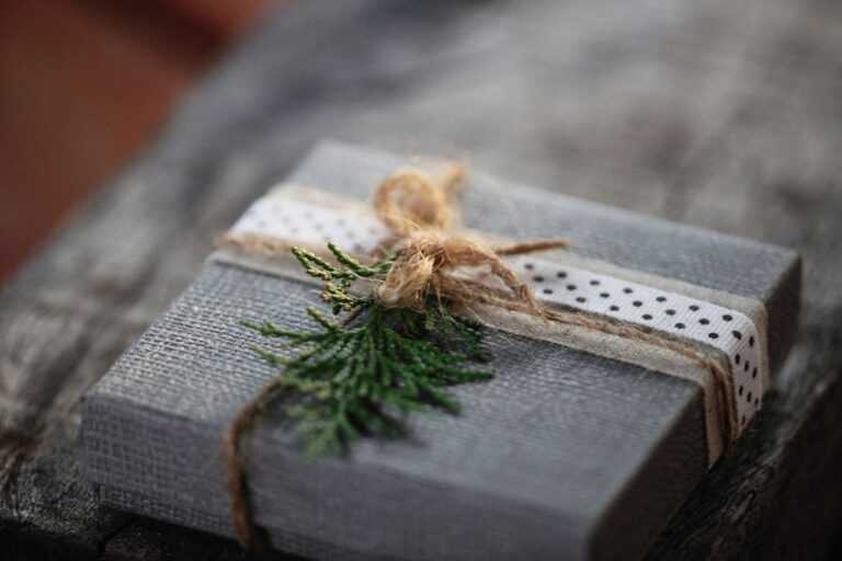A rustic gift box wrapped with twine and decorated with greenery on a wooden surface.